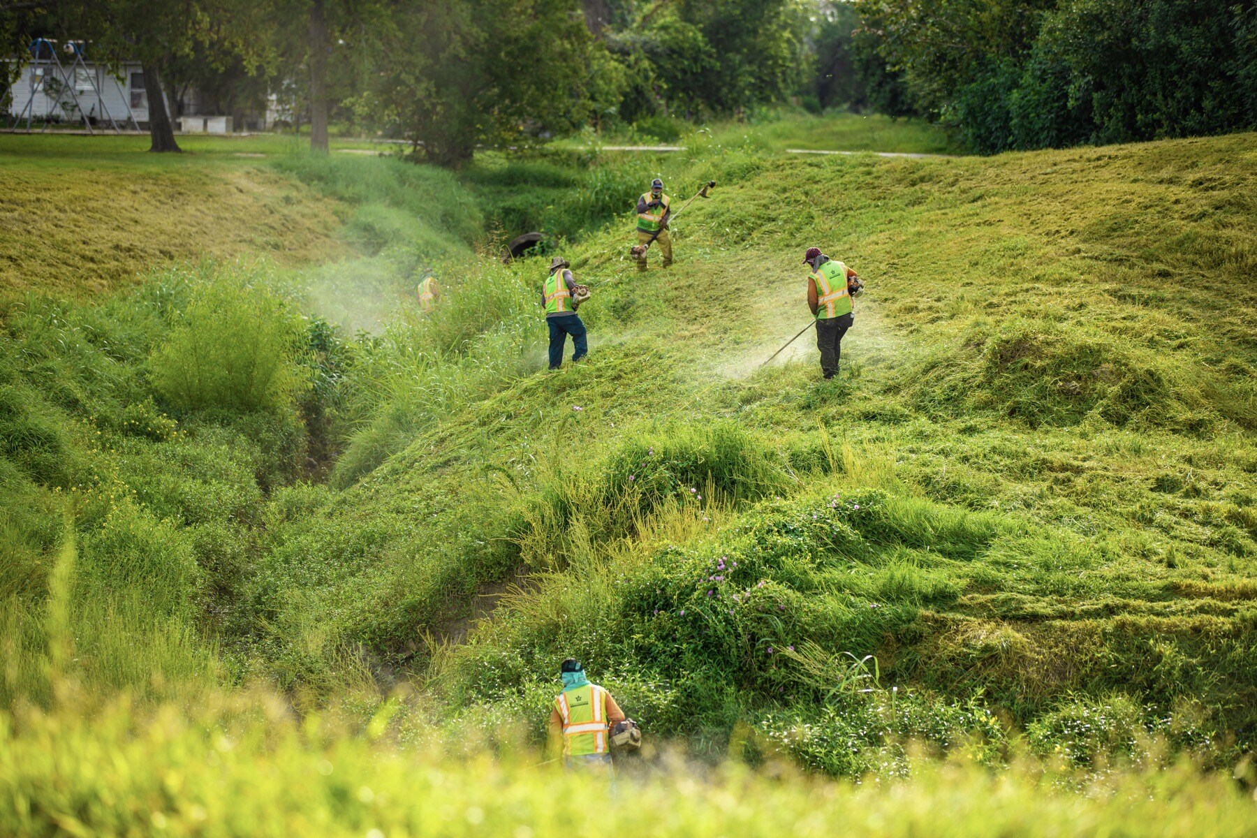 landscape employees string trimming in flood control area